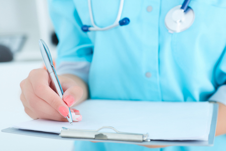 Female medicine doctor hand holding silver pen writing something on clipboard closeup.の写真素材