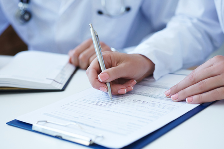 Healthcare or insurance concept. Female doctor filling medical form while consulting patient. Just hands over the table.の写真素材
