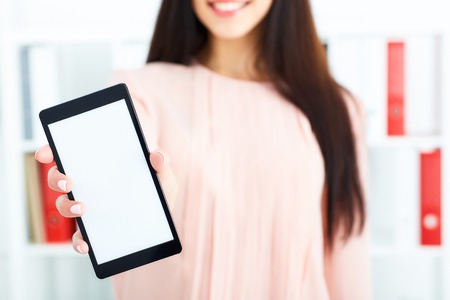 Young brunette holding a smartphone with blank screen. Business, exchange market, job offer, analytics research, excellent education, certified public accountant concept.の写真素材