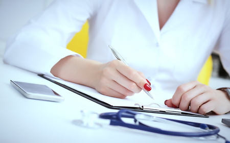 Female medicine doctor hand holding silver pen writing something on clipboard and working laptop closeup. Physician ready to examine patient and helpの写真素材