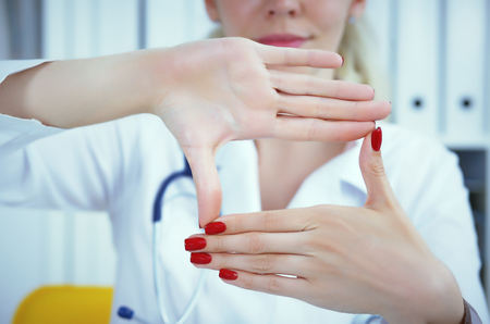 Young female doctor holding hands with advertising area between them and smiling on medical office in background. Photo with depth of fieldの写真素材