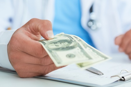 Male medicine doctors hand holding two hundred dollars banknotes closae-up. Medic personnel salary, prestige and high paid job, education, public health business, medical insurance concept.の写真素材