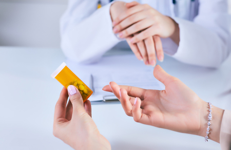 Female medicine doctor hand hold jar of pills and explain how to take pills to patient at worktable. Panacea and life save prescribing treatment legal drug store concept.の写真素材