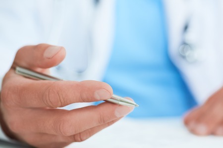 Closeup of male doctors hands taking notes or fills in the clients medical card or prescribes medication. Ward round, patient visit check, medical calculation and statistics concept.の写真素材