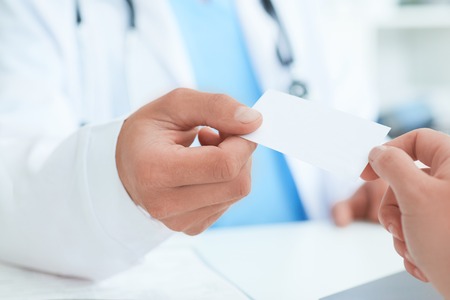 Male doctors hand give white blank calling card to woman closeup in office. Physical, disease prevention, examine patient, instrument shop, healthy lifestyle, family doctor conceptの写真素材