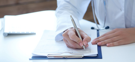 Close-up view of female doctor hands filling patient registration form. Healthcare and medical concept.の写真素材