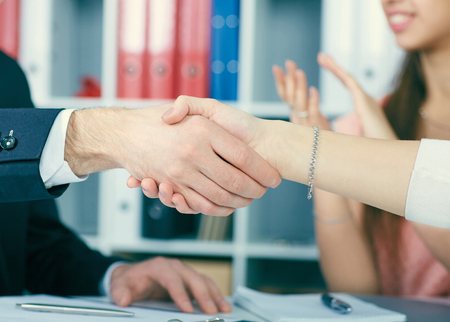 Close up business people handshake on team meeting with clapping group of people blured in background at modern startup business office interior.の写真素材