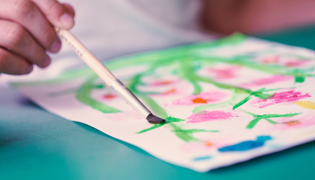 Close-up of a brush in the hand of a little child drawing flowers with colorful watercolors. School, education concept.の写真素材