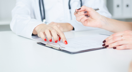 Female patient at reception of doctors office filling out medical form. Just hands over the table.の写真素材