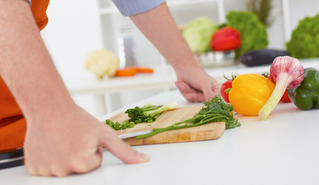 Healthy eating, cooking, vegetarian food, dieting and people concept - close up of man chopping green onion with knife on wooden cutting board.の写真素材