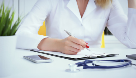 Female medicine doctor hand holding silver pen writing something on clipboard and working laptop closeup. Physician ready to examine patient and helpの写真素材