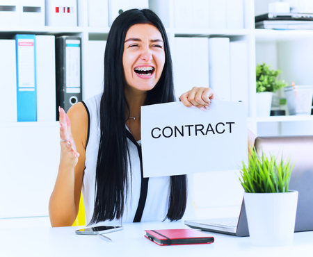 Young angry business woman ripping contract at the desk, break the rules - failure business concept.の写真素材