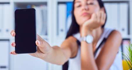 Young sad woman showing a blank smartphone screen. Focus on smartphone. Free space for your message.の写真素材
