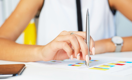 Female hand point silver pen to business graph on seminar. Bank credit, loan money, invest, tax situation review, income calculation form concept.の写真素材