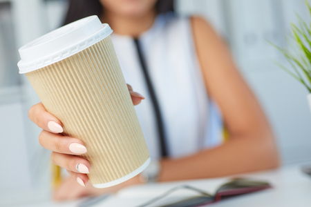 Girl showing paper cup of coffee in his hands close up. American paper eco cup. Girl drinking coffee indoors.の写真素材