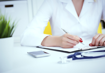 Female medicine doctor hand holding silver pen writing something on clipboard and working laptop closeup. Physician ready to examine patient and helpの写真素材