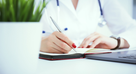 Female medicine doctor hand holding silver pen writing something on clipboard and working laptop closeup. Physician ready to examine patient and helpの写真素材