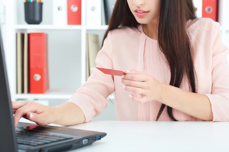 Young woman holding credit card in hand and entering security code using laptop keyboard. Internet banking concept.の写真素材