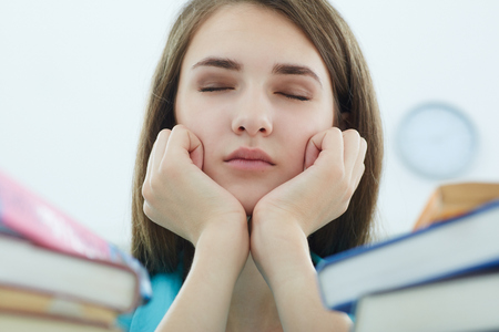 Tired student girl or young woman with books and coffee sleeping in libraryの写真素材