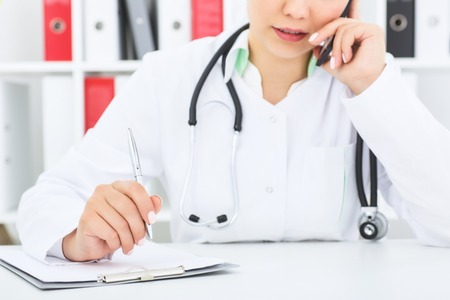 Middle section of female medical doctor making telephon call.の写真素材