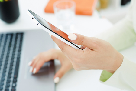 Girl hand holding smart phone. Stylish modern office workplace on a background.の写真素材