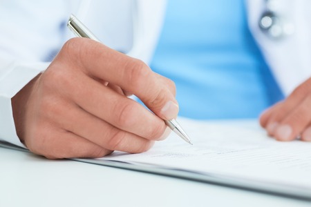 Closeup of male doctors hands taking notes or fills in the clients medical card or prescribes medication. Ward round, patient visit check, medical calculation and statistics concept.の写真素材