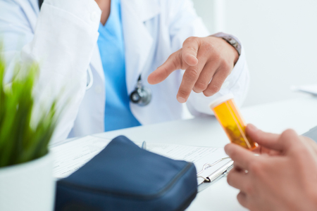 Bottle of pills in the hands of the patient close-up. Male doctor gesticulating explains how to take the drug in the background.の写真素材