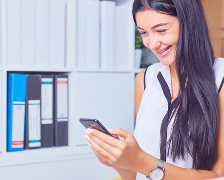 Business woman holding smartphone in hands and smile in the office.の写真素材