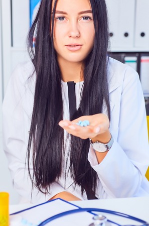 Young business woman taking medicine in a stressful situation at workplace. Woman consults on the phone with her doctor about taking medicationの写真素材