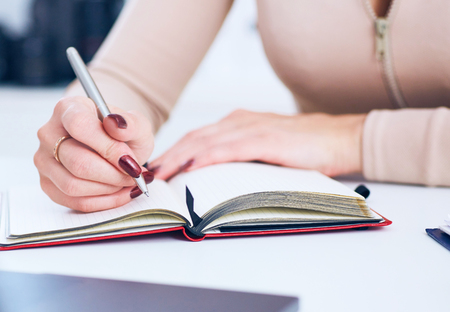 Close up of a businesswoman hands writing in a document on a desktop at office.の写真素材