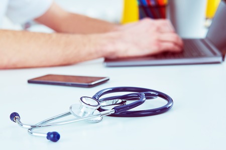 Stethoscope with smartphone and laptop on the desk. Male doctor working in hospital writing a prescription, Healthcare and medical concept.の写真素材