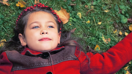 Season and people concept. Little girl in a red coat lying on the ground covered with yellow autumn leavesの写真素材