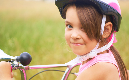 Portrait of a playful funny little girl in a pink safety helmet on her bikeの写真素材