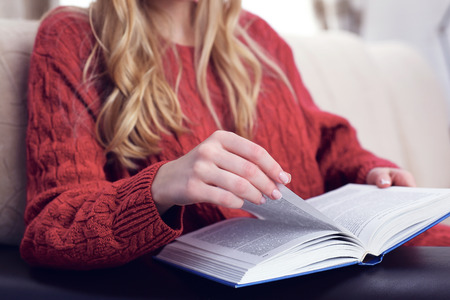 Middle section of young woman reading book at home interior backgroundの写真素材