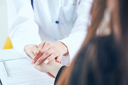 Friendly female doctors hands holding female patients hand for encouragement and empathy close-up. Partnership, trust and medical ethics concept.の写真素材