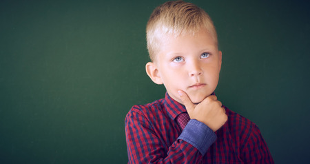 Closeup shot of schoolboy thinking with hand on chin isolated on blackboard. Portrait of pensive...