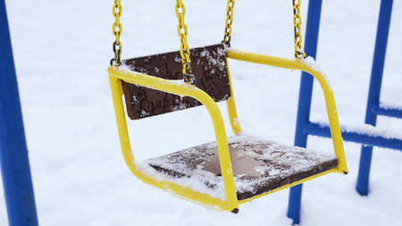 Children swing in park under the snow after the strongest snowfall. Frozen swing in December.