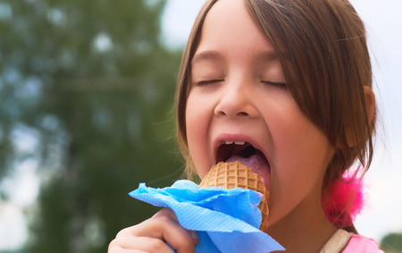 Pretty little girl eating licking big ice cream in waffles cone happy laughing on nature backgroundの写真素材