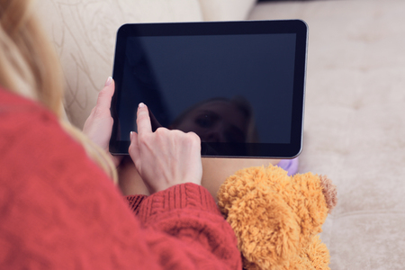 Young woman watching media content showing a blank tablet screen sitting on a sofa at home. Girl studying online content using a tablet at homeの写真素材