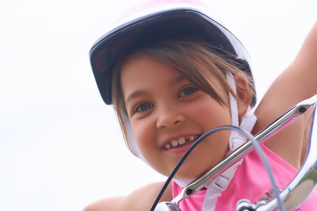 Portrait of a litte Cacasian girl in a pink safety helmet driving her bike.の写真素材