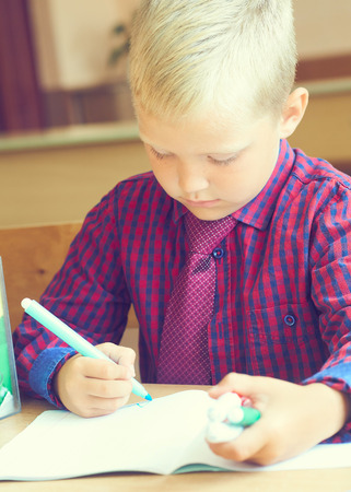 Boy is painting a picture. A beautiful child with felt-tip pens sits at the table and is engaged in creativity and art. Drawing in kindergarten, school.の写真素材