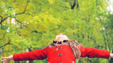 Portrait of little girl with arms outstretched outdoors in autumn public park.の写真素材