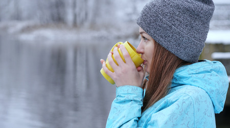 Pretty Caucasian girl dreaming looking into the distance standing outdoor with cup of tea near...