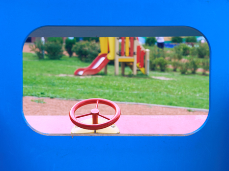 Wooden toy car in the playground for children. Red metal steering wheel of childrens wooden car on the playground closeup.の写真素材