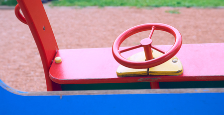 Wooden toy car in the playground for children. Red metal steering wheel of childrens wooden car on the playground closeup.の写真素材