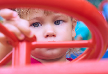 Little Caucasian baby girl sits at the wheel of a toy car. Playing on the playground concept.の写真素材