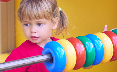 Little Caucasian girl in red tshirt playing with abacus on playground outdoors in summer day.の写真素材