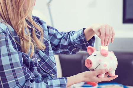 Young girl sitting on couch and putting litecoin in piggybank.の写真素材