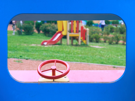 Wooden toy car in the playground for children. Red metal steering wheel of childrens wooden car on the playground closeup.の写真素材