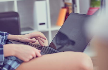 Beautiful young blond woman working on a laptop sitting on the comfortable sofa at home. Freelance or lifestyle concept.の写真素材